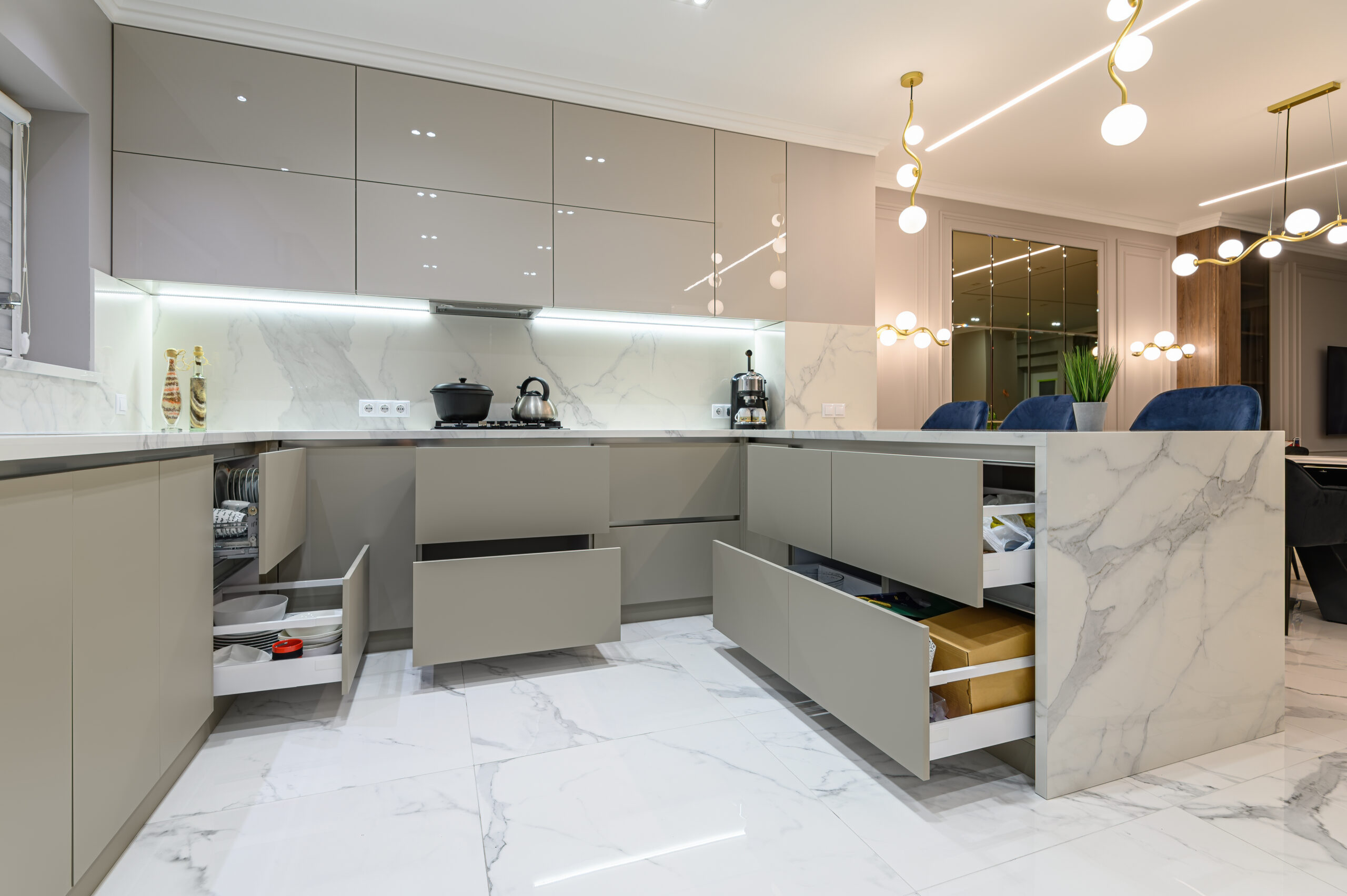 Open drawers at well designed large modern white wood and marble kitchen united with living room as a pert of studio flat